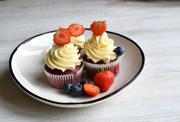Delicious plate of cupcakes with berries on white wooden surface. Red velvet cupcakes.