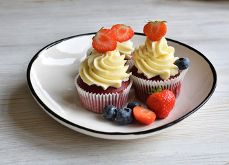 Delicious plate of cupcakes with berries on white wooden surface. Red velvet cupcakes.