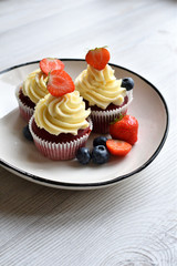Delicious plate of cupcakes with berries on white wooden surface. Red velvet cupcakes.