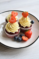 Delicious plate of cupcakes with berries on white wooden surface. Red velvet cupcakes.