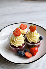 Delicious plate of cupcakes with berries on white wooden surface. Red velvet cupcakes.