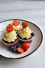 Delicious plate of cupcakes with berries on white wooden surface. Red velvet cupcakes.