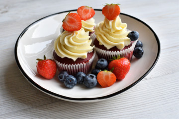 Delicious plate of cupcakes with berries on white wooden surface. Red velvet cupcakes.