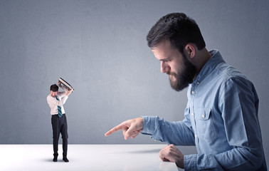 Young professional businessman being angry with an other miniature businessman in front of a blueish grey background