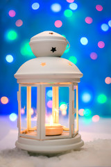 Christmas lantern in the snow on a magical blurred background with lights