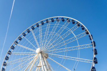 Low angle view of white structure and blue cabin of Ferris wheel with background of clear blue sunny sky.