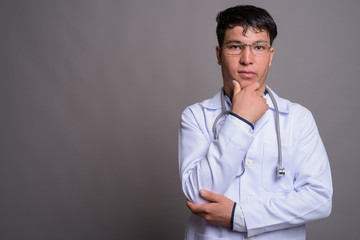 Young Asian man doctor against gray background