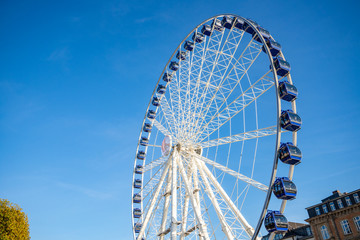 Low angle view of white structure and blue cabin of Ferris wheel with background of clear blue sunny sky.