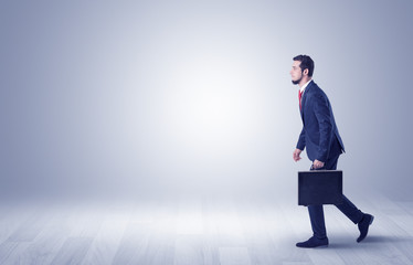 Successful businessman walking in front of an empty wall with briefcase on his hand
