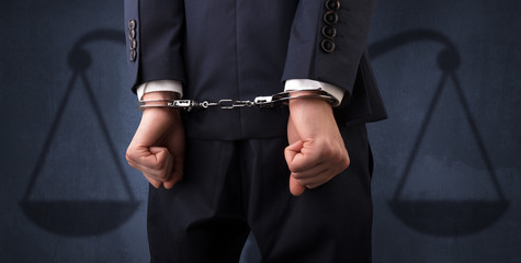 Arrested businessman in handcuffs with hands behind back and justice symbol wallpaper
