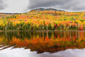 Fototapeta premium Fall colors of Lac Legault with Mont Kaaikop in the background, in cottage country in the Laurentians, Quebec, Canada.