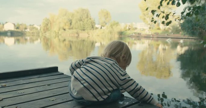 Little toddler sitting on pier by lake
