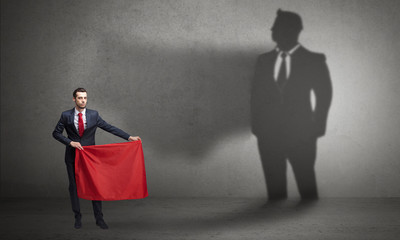 Businessman standing with red cloth on his hand and his shadow on the background
