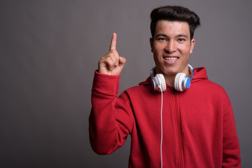 Young Asian man wearing headphones against gray background