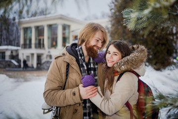 Young loving couple Caucasian man with blond long hair and beard, woman with toothy smile have fun, indulge, fool around winter park near Christmas tree, coniferous tree after ice skating in winter