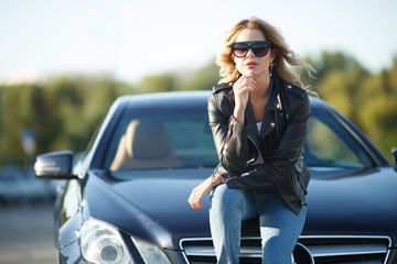 Photo of young woman in sunglasses sitting on hood of black car