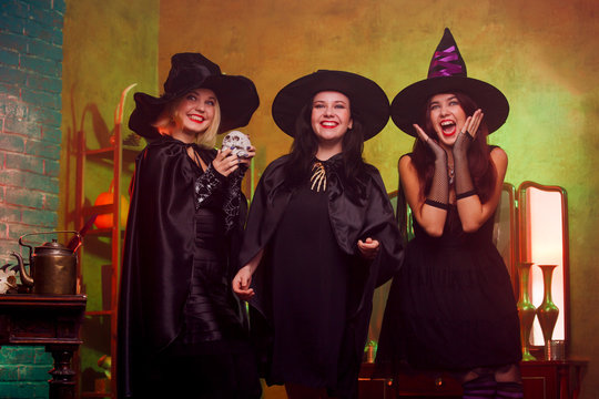 Picture of three witches in black hats in dark room against mirror and rack