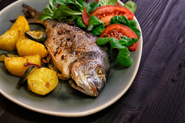  Meal.Baked Dorado fish with vegetables in the oven on a dark background.