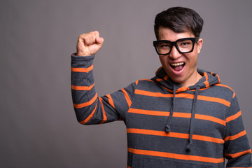 Young Asian nerd man wearing hoodie against gray background