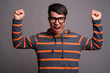 Young Asian nerd man wearing hoodie against gray background