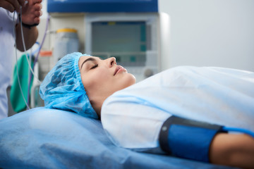 Pretty young lady wearing medical clothes and lying with her eyes closed at the surgery