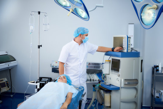 Smart experienced anesthesiologist standing next to his patient and looking at the screen while preparing the narcosis