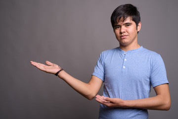 Young Asian teenage boy wearing blue shirt against gray backgrou