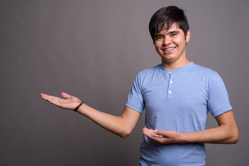 Young Asian teenage boy wearing blue shirt against gray backgrou