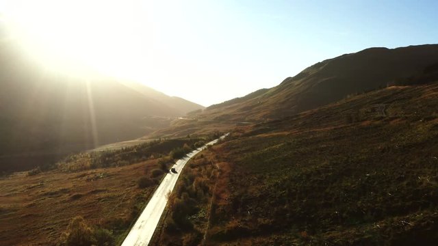 Cars driving on a mountain road at sunrise in the Scottish highlands, UK.