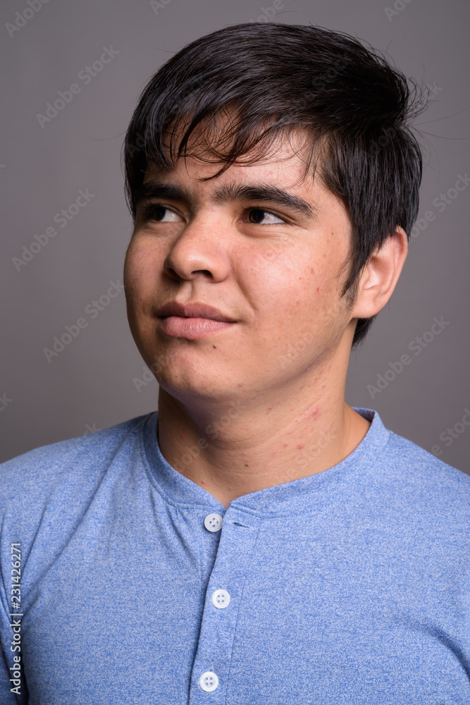 Wall mural Young Asian teenage boy wearing blue shirt against gray backgrou