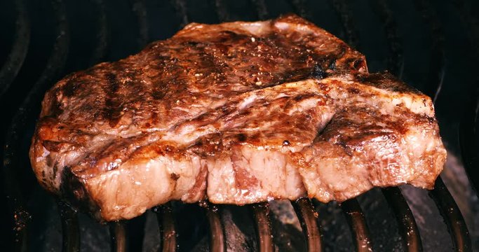 C4K closeup shot of the seasoned t-bone steak on a barbecue grill
