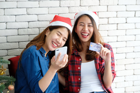 Two young cute asia women holding smartphone and credit card for shopping online background, mock up, with happiness, Christmas holiday shopping concept