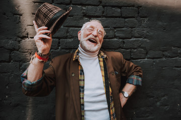 Waist up portrait of stylish expressive pensioner with joyful smile taking off his hat