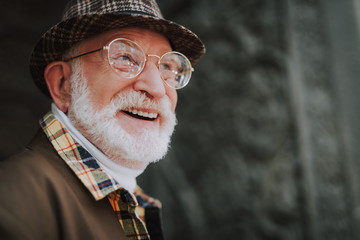 Close up portrait of good looking old male with white beard and joyful glance having good day and...