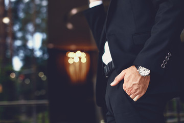 Attractive young man in dark suit and with a watch on his wrist putting his hand into the pocket of his trousers © Yakobchuk Olena