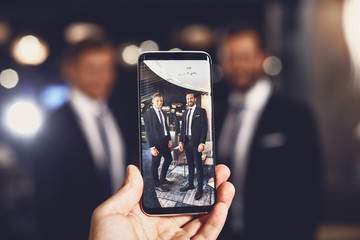 Photo together. Happy young elegant man taking photo together with a help of modern smartphone