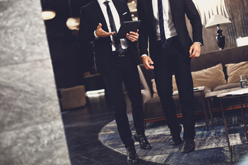 Two elegant business partners having meeting in the hall and using modern tablet