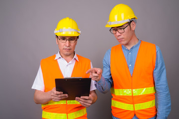 Two young Asian men construction worker together against gray ba