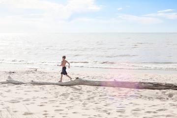 Fototapeta na wymiar Boy running on a piece of driftwood on the beach