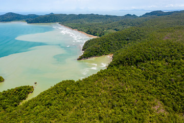 Aerial drone view of dense tropical rainforest leading to a remote, rough ocean coastline