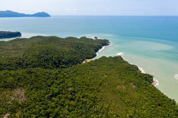 Aerial drone view of dense tropical rainforest leading to a remote, rough ocean coastline