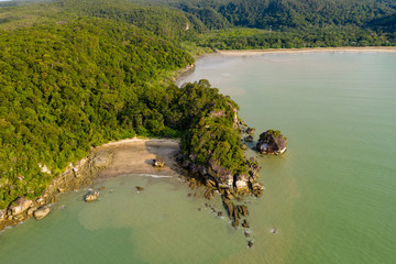 Aerial drone view of a beautiful small, deserted sandy beach in a small bay surrounded by tropical rainforest