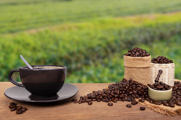 Hot cup of coffee and beans with burlap sack on the wooden table, at the coffee plantations background with copy space