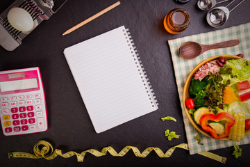Dieting and nutrition. Diet plan, tape measure, calculator for Count calories,  salad healthy food on black stone background. Weight loss. Copy space.