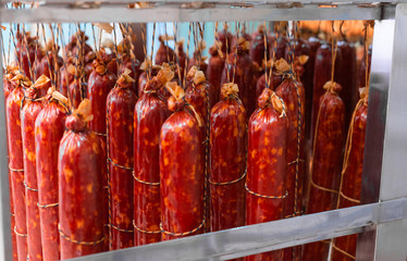 Smoked sausage suspended on a rope on a metal frame in the smokehouse.