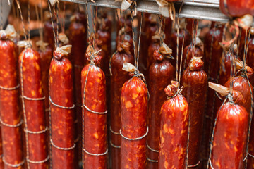 Smoked sausage suspended on a rope on a metal frame in the smokehouse.