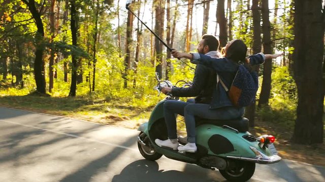 Happy couple riding and taking silfie video on a scooter in the forest. Sunny beautiful day.