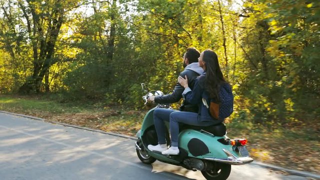 Happy couple riding a scooter in the forest. Sunny beautiful day.