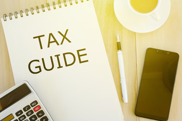 Top view of mobile phone,calculator,a cup of coffee,pen and notebook written with Tax Guide on...