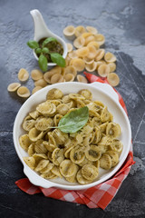 Italian orecchiette served with basil pesto sauce in a white plate, vertical shot on a grey...